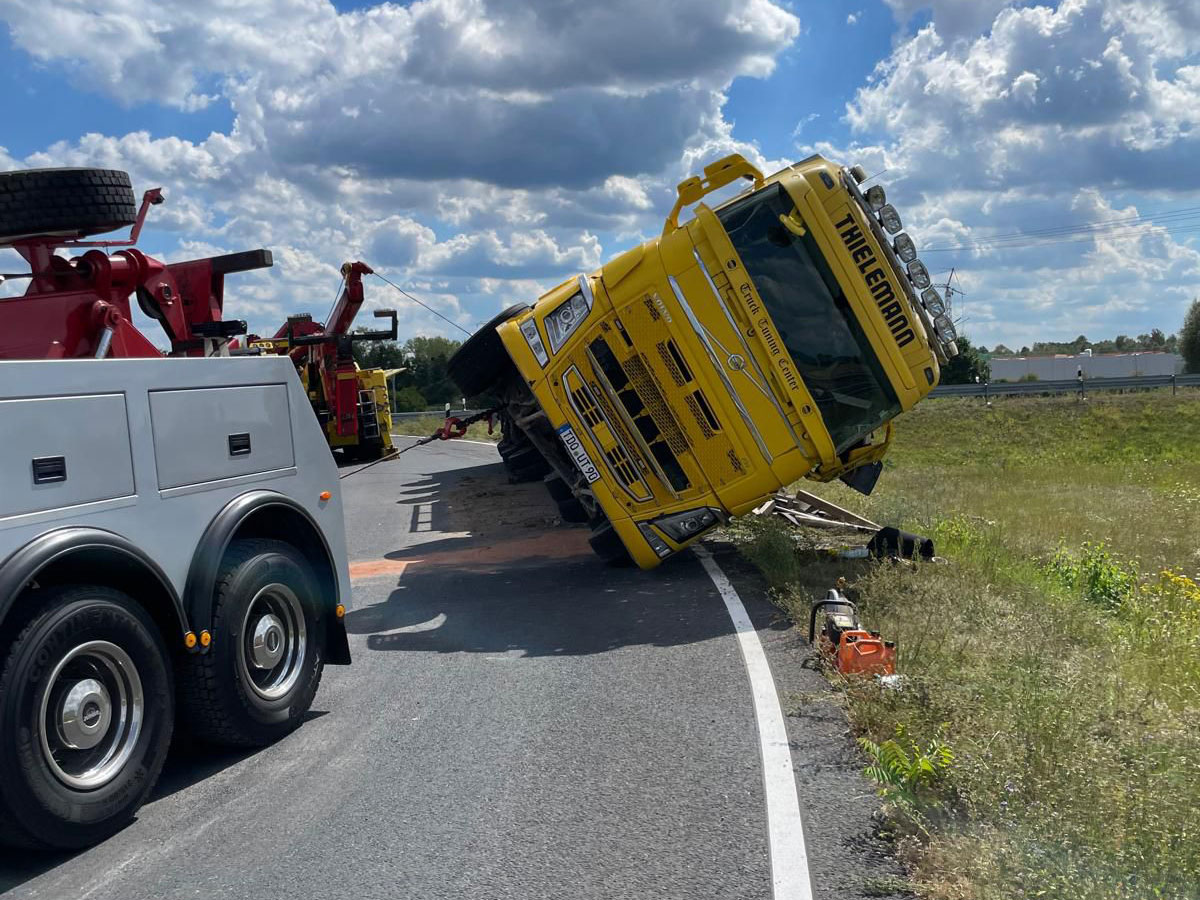 Truck accident recovery in action: heavy-duty towing service safely uprights an overturned truck at the roadside using crane and winch.